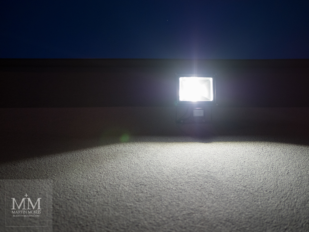Svítící lampa na zdi. Fotografie zhotovená objektivem Olympus M. Zuiko digital ED 25 mm 1:1.2 Pro.