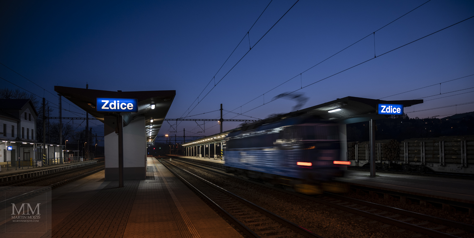 A locomotive passes through a station at dusk.