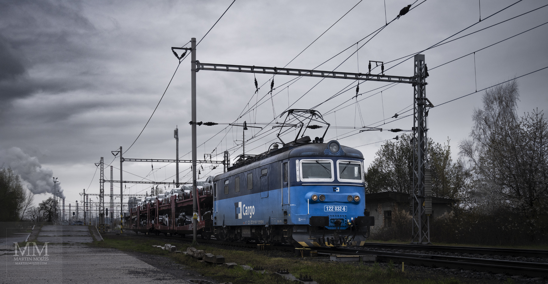 Lokomotiva 122 032-6 v čele nákladního vlaku přepravujícího automobily.