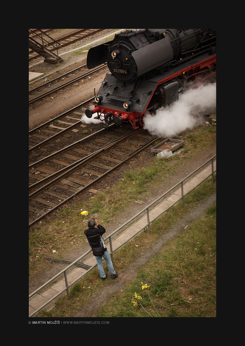 Fotograf fotografuje projíždějící parní lokomotivu.