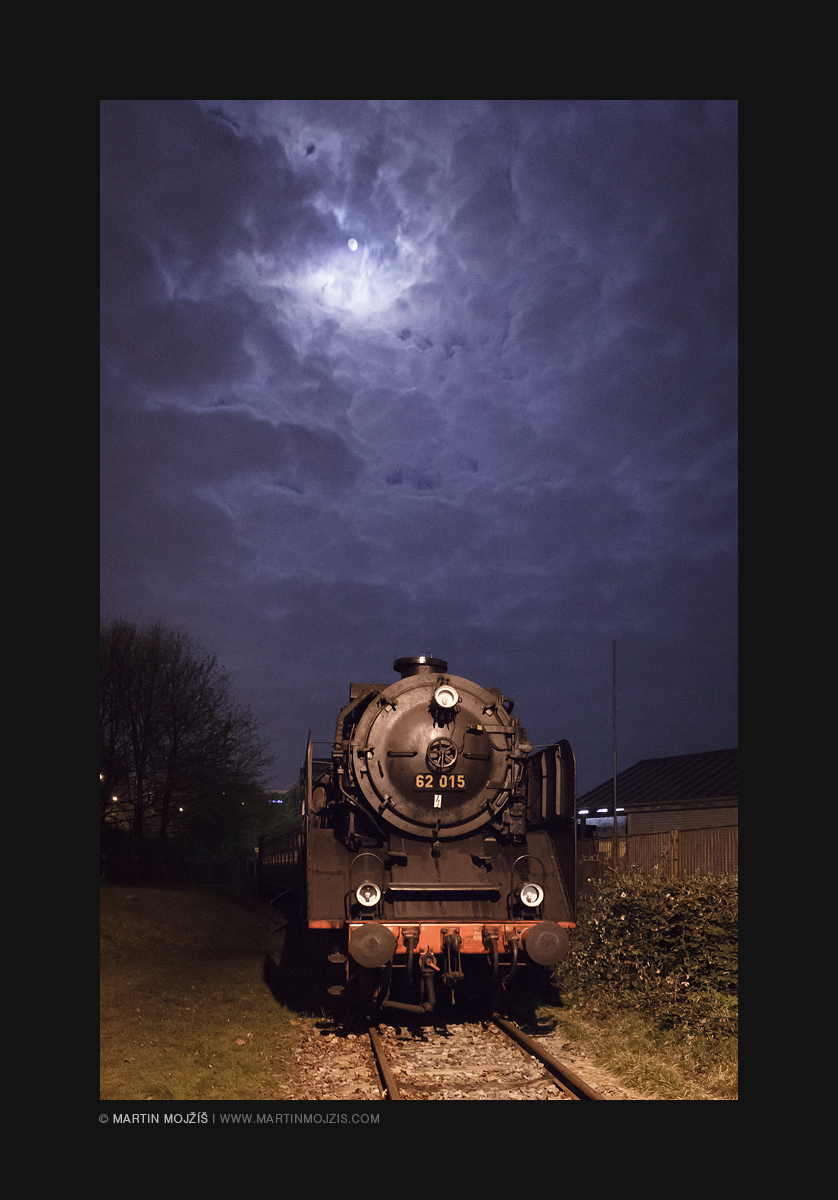 Parní lokomotiva pod nebem se svítícím Měsícem.