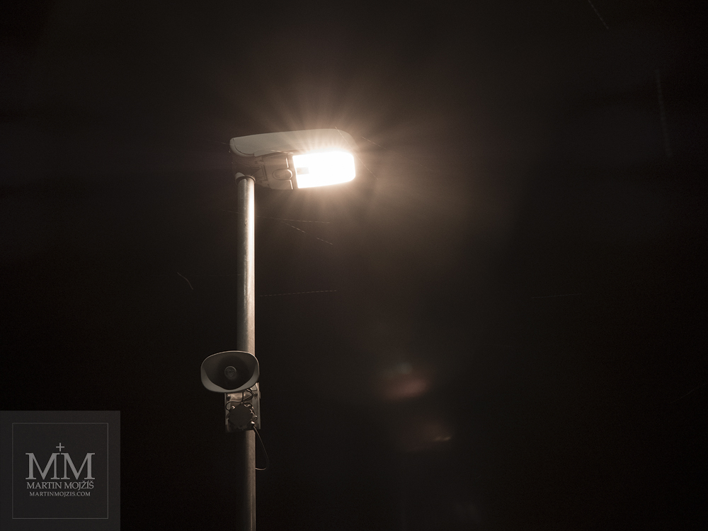 Svítící lampa na železničním nástupišti, padající sníh, odlesky. Fotografie zhotovená objektivem Olympus M. Zuiko digital ED 25 mm 1:1.2 Pro.