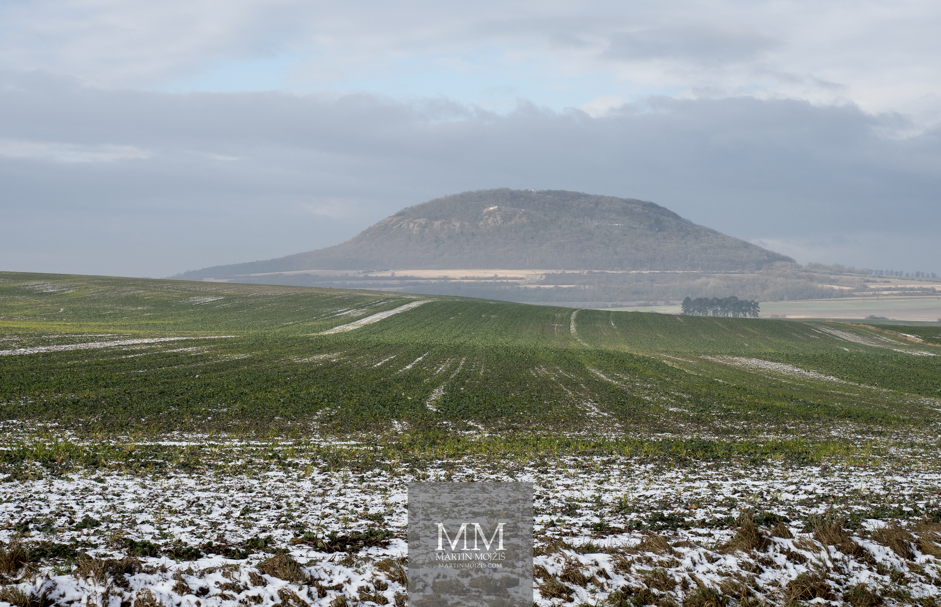 Hora Říp v zimě, v popředí mírně zasněžené pole. Fotografie vytvořená fotoaparátem Olympus OM-D E-M1 Mark II.