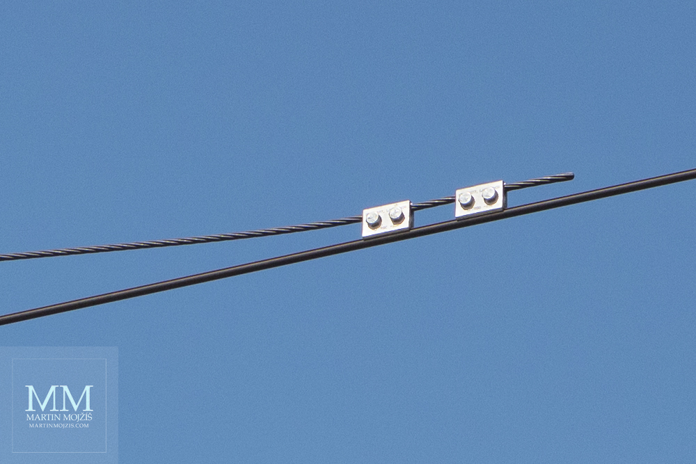 Výřez z fotografie železničního trolejového vedení a modrého nebe, zhotovené objektivem Canon EF 50 mm 1:1.8 STM.