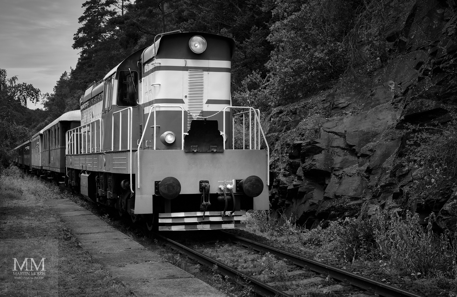 Velkoformátová umělecká černobílá fotografie dieselové lokomotivy v čele osobního vlaku. Martin Mojžíš.
