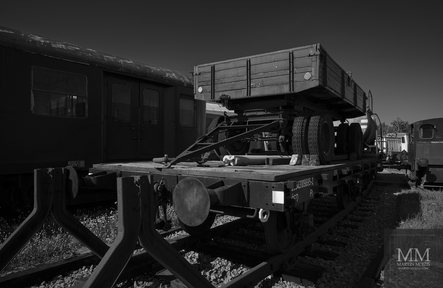 A road flatbed loaded on a railway platform wagon. Black and white fine art photograph REST IN THE MIDDLE OF SUMMER I, photographed by Martin Mojzis.