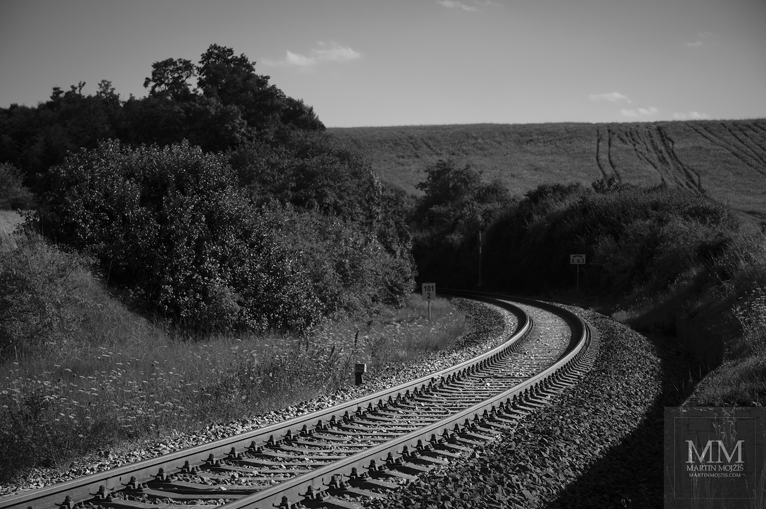 Železniční trať v oblouku mezi poli. Umělecká černobílá fotografie s názvem OBLOUK A POLE. Fotograf Martin Mojžíš.