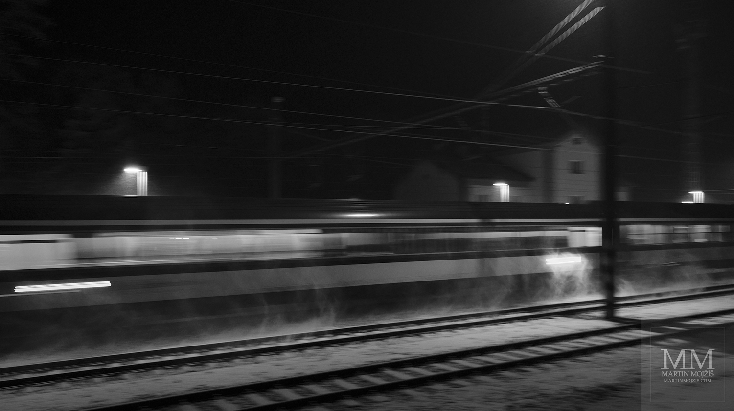 Noční vlak jedoucí po osvětlené zasněžené trati. Umělecká černobílá fotografie s názvem ZASNĚŽENOU NOCÍ II. Fotograf Martin Mojžíš.