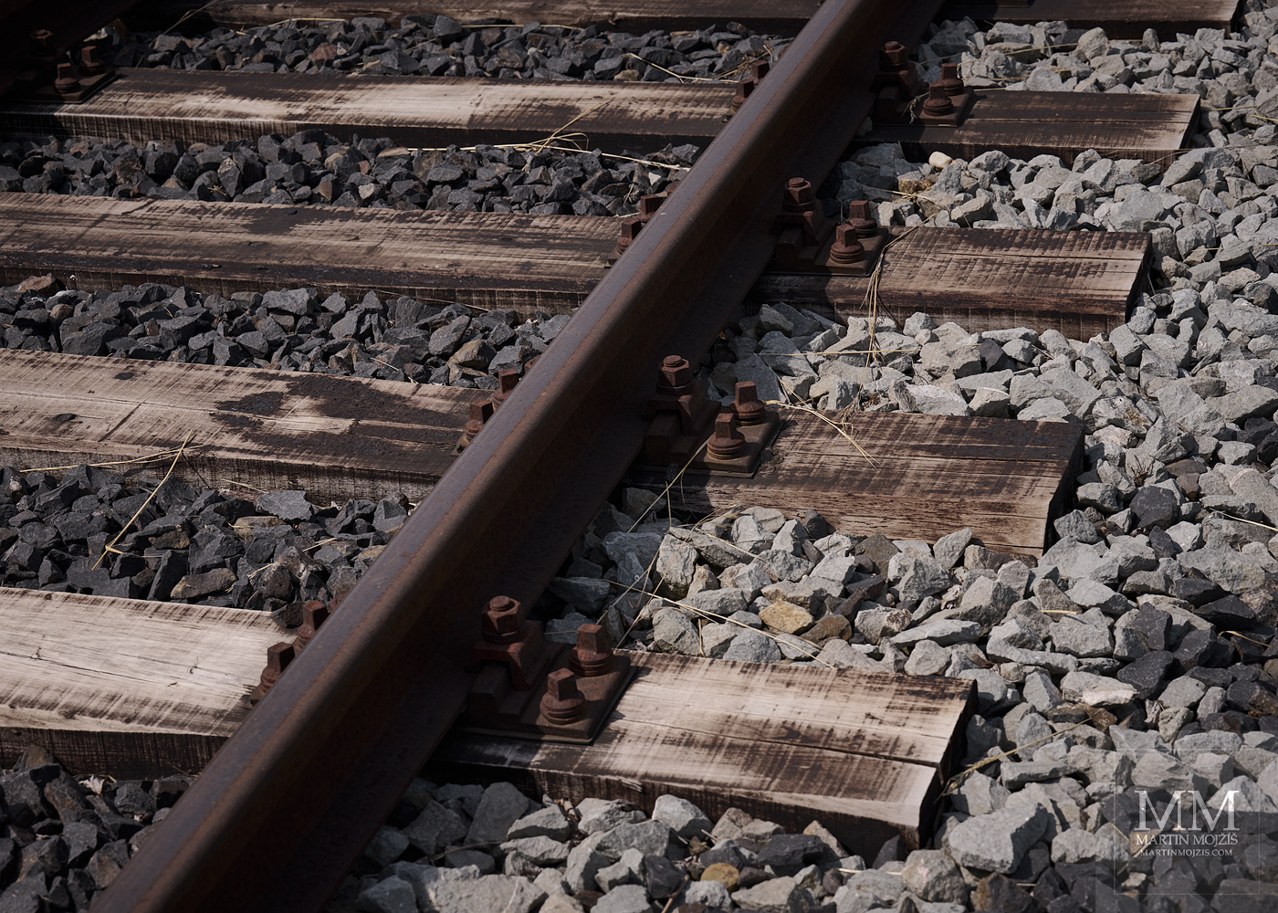 Železniční koleje, dřevěné pražce a štěrkové lože. Umělecká fotografie s názvem DŘEVO, KOV A KÁMEN. Fotograf Martin Mojžíš.