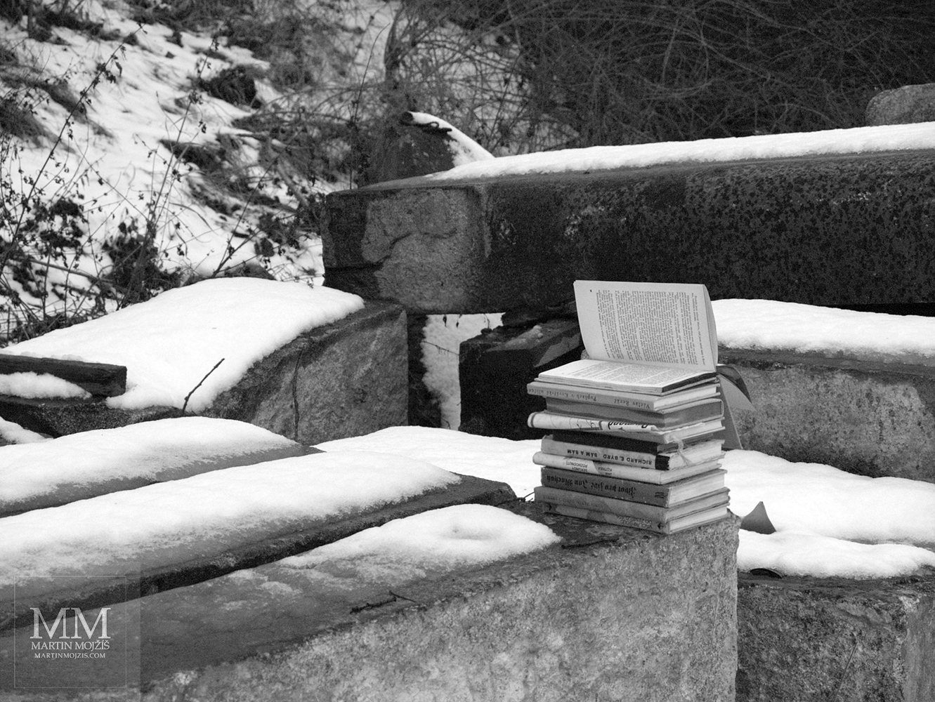 Knihy odložené venku na velkém kamenném kvádru, místy sníh. Fotografie s názvem KNIHY.