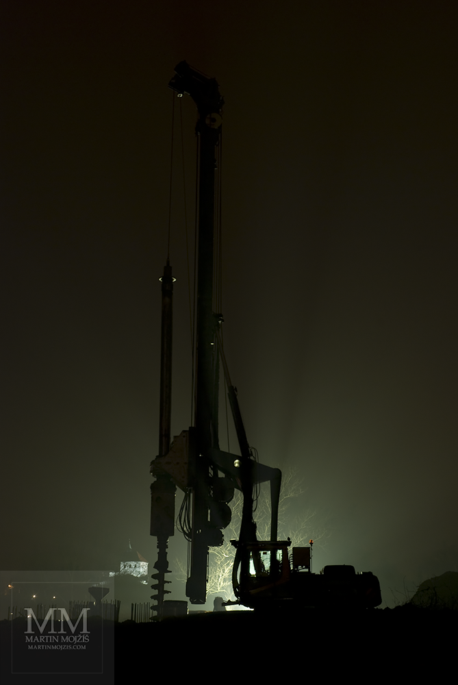 Ground drilling machine, in the background a chapel. Fine Art photograph of Martin Mojzis with the title OPPOSITE VERTICAL DIRECTION IN ONE FEBRUARY NIGHT.