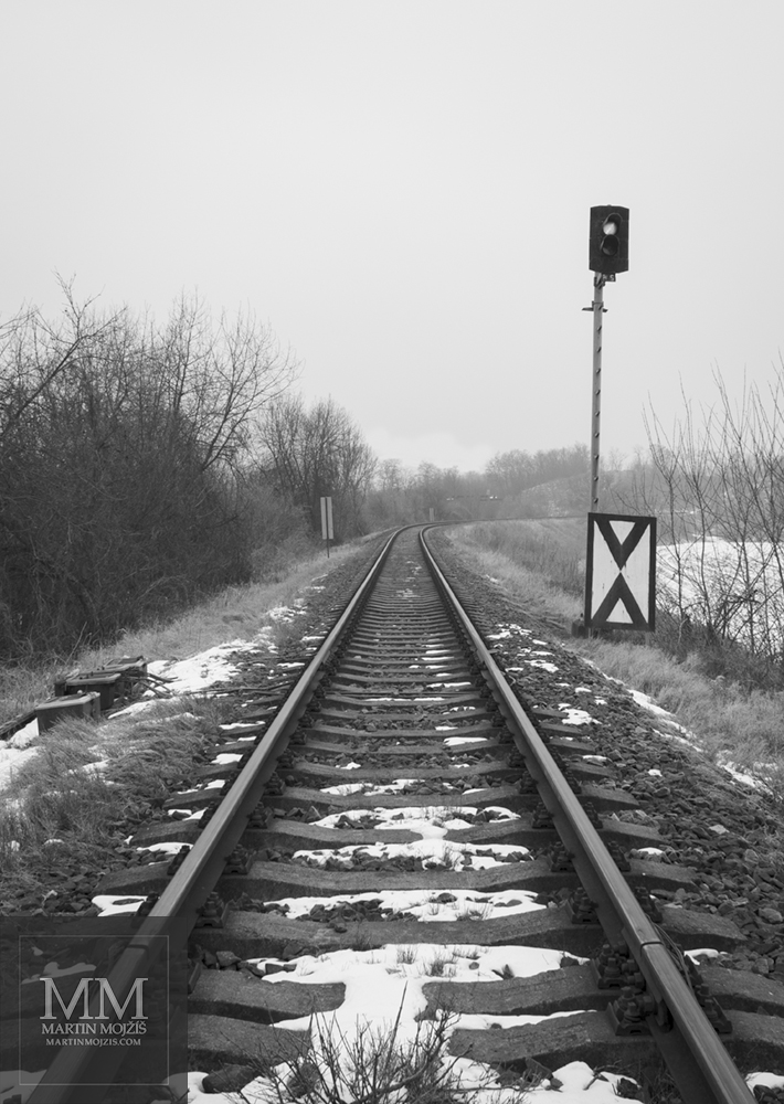 Railway track in winter, signalling light on the right side. Fine Art black and white photograph of Martin Mojzis with the title ON THE COMMENCENMENT OF WAYS.