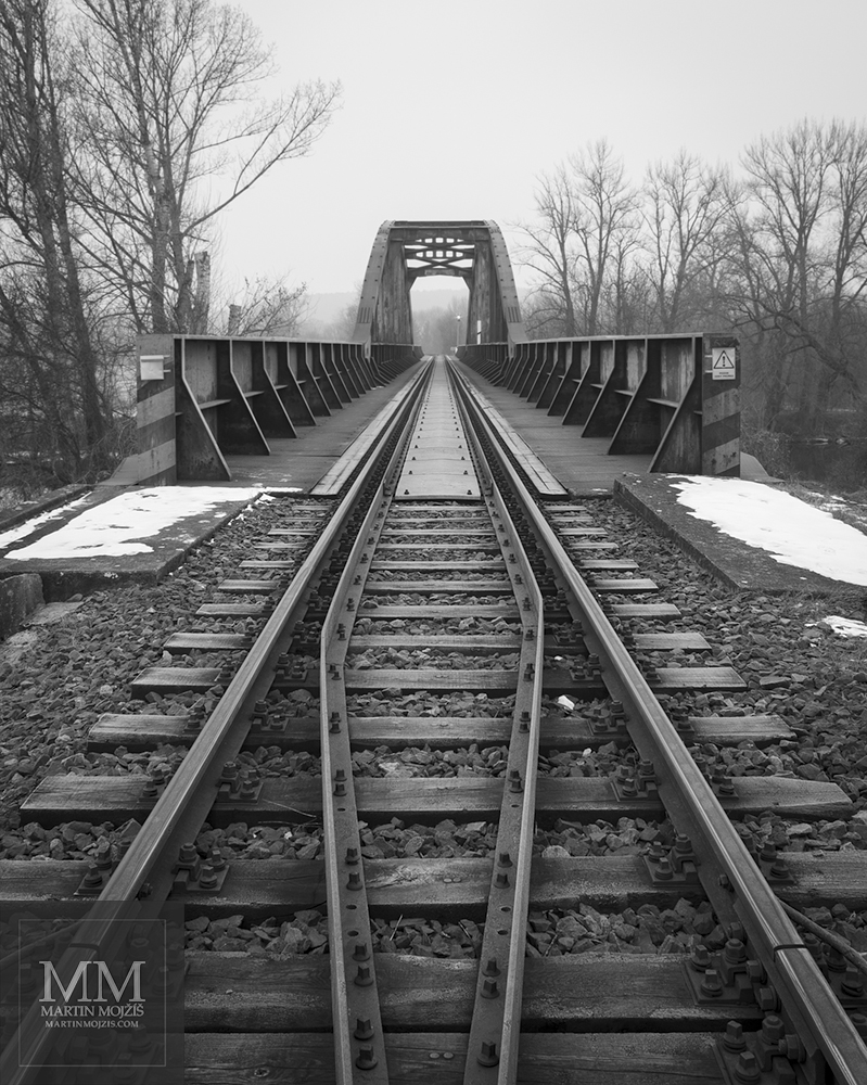 Pohled na přídržnice v jednokolejné trati před vjezdem na most. Umělecká černobílá fotografie Martina Mojžíše s názvem TICHO.