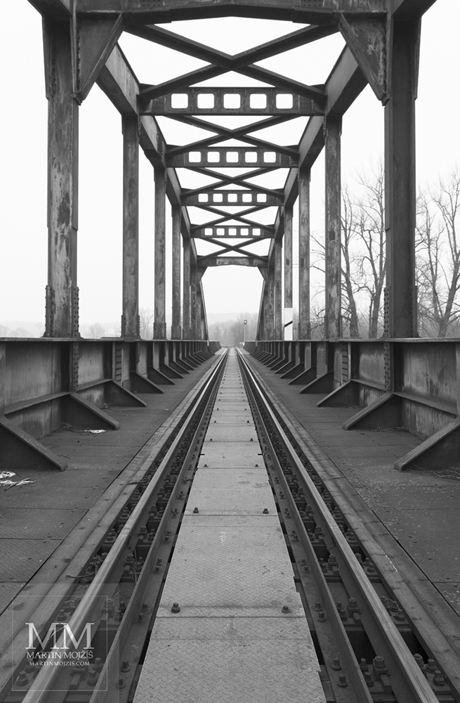 Konstrukce ocelového železničního mostu v pohledu na výšku. Umělecká černobílá fotografie Martina Mojžíše s názvem V LEDNOVÉM ODPOLEDNI.