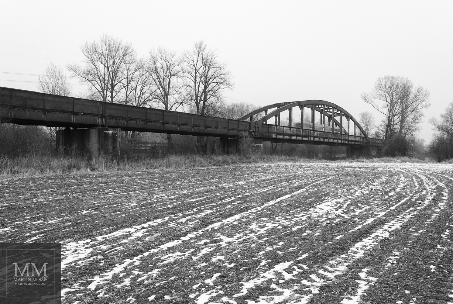 Černobílá umělecká fotografie zimní krajiny s ocelovým železničním mostem s názvem ROKY A CESTY. Fotograf Martin Mojžíš.