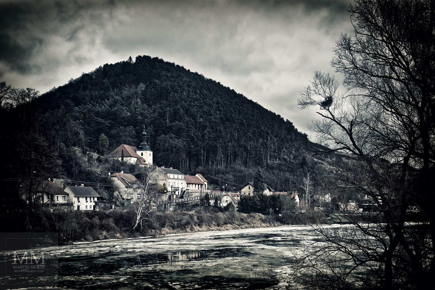 Řeka plná ledových ker ve vesnici, kostel, tmavé mraky.