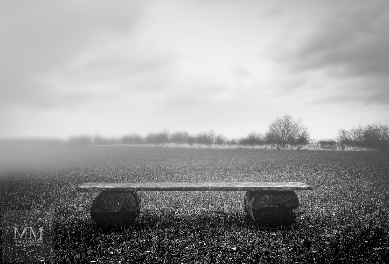 Dřevěná lavička na poli, mlha. Černobílá fotografie.