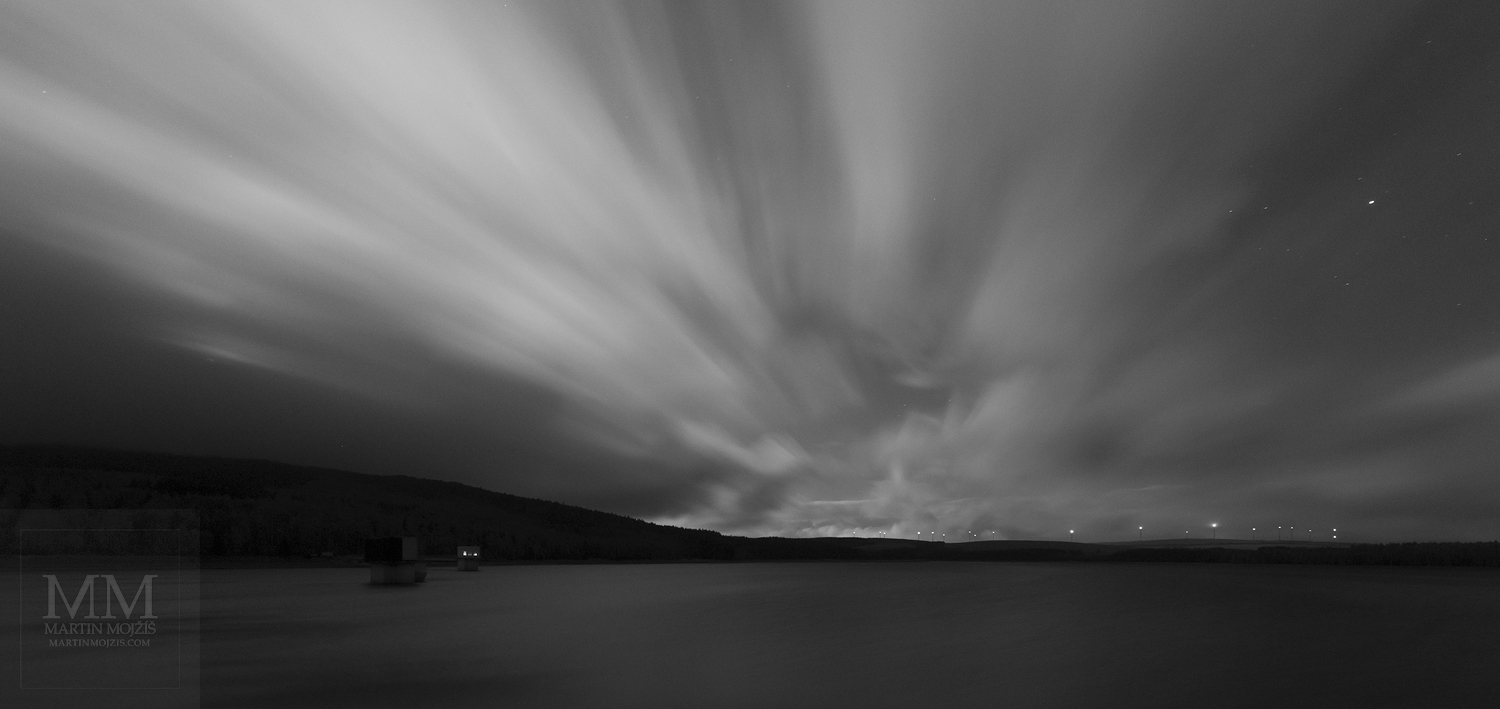 Velkoformátová umělecká fotografie noční krajiny s letícími mraky nad jezerem. Martin Mojžíš.
