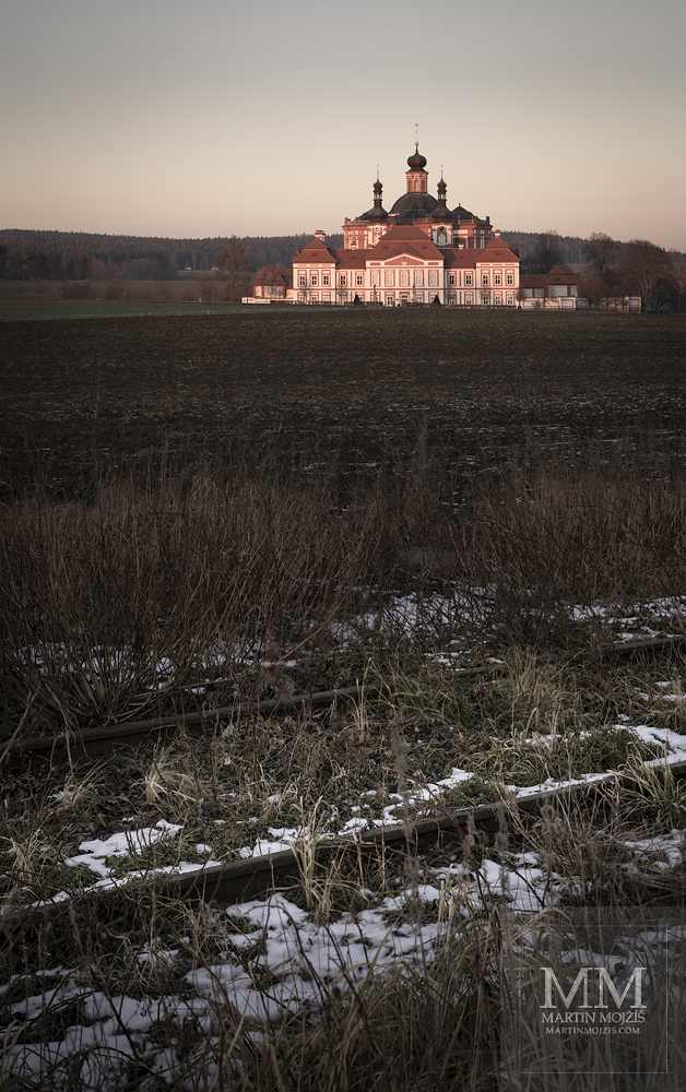Mariánská Týnice v zimě, v popředí železniční trať a pole. Umělecká velkoformátová fotografie Svědectví minulých cest. Fotograf Martin Mojžíš.