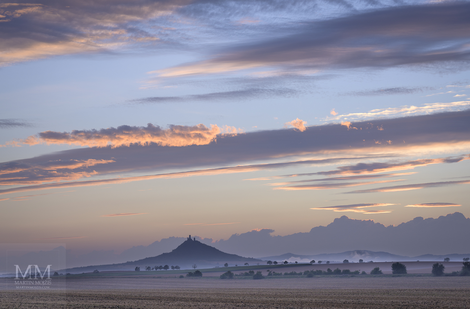 Krajina s večerními mlhami, v pozadí vrch Hazmburk (Klapý). Umělecká velkoformátová fotografie Letní den již usíná. Fotograf Martin Mojžíš.