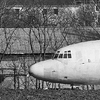 The front part of a large white airliner in a farm field.